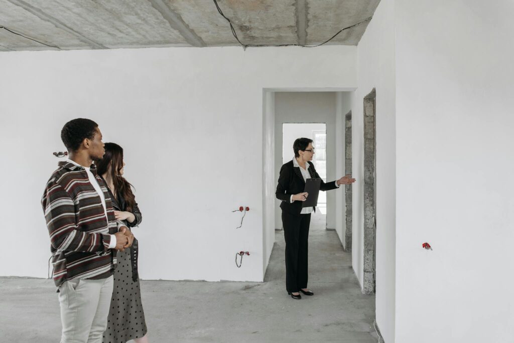 A couple explores an unfinished apartment with a real estate agent, considering property purchase options.