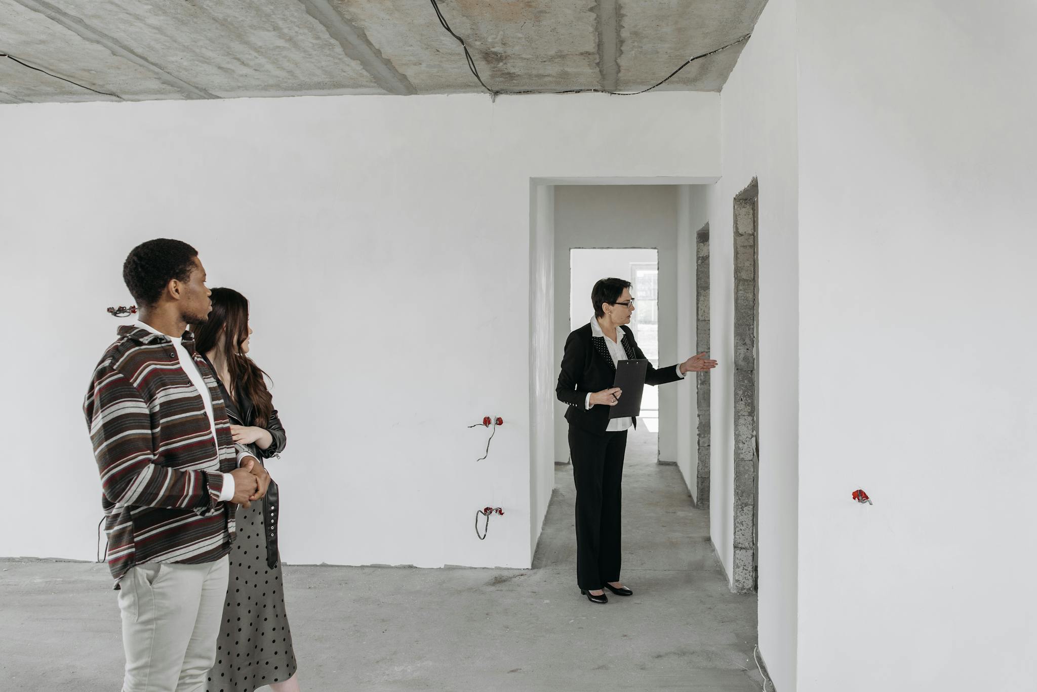 A couple explores an unfinished apartment with a real estate agent, considering property purchase options.